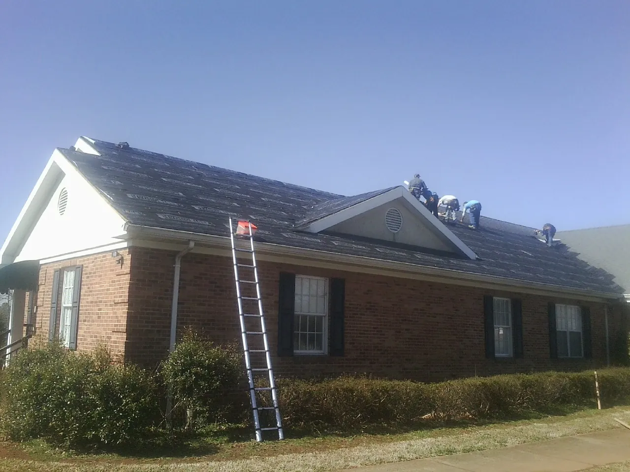 Crew tearing shingles off a brick ranch roof with a ladder set — Metal Roof Repair work by our crew in White Plains