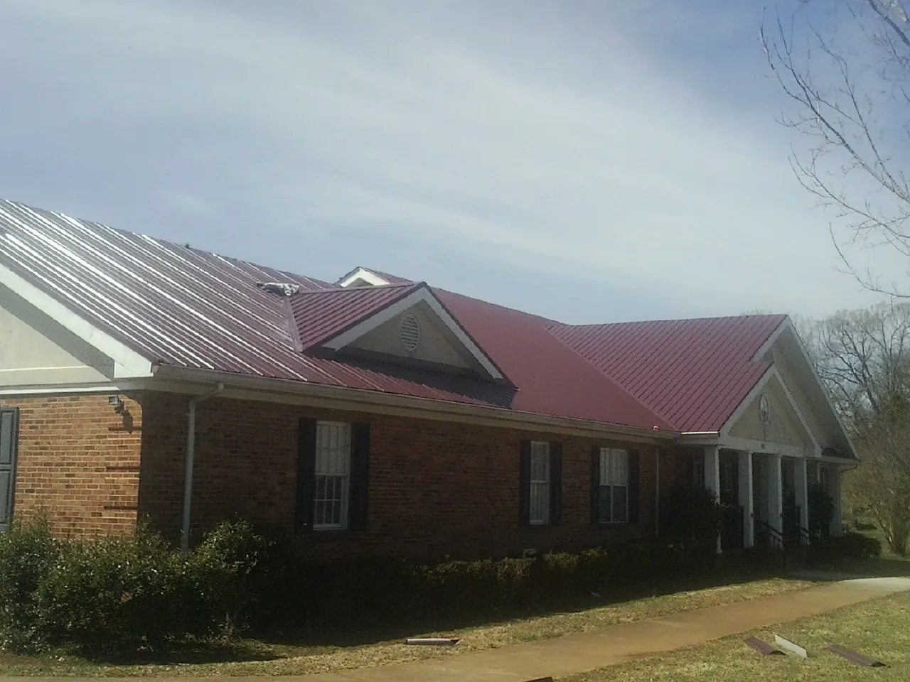 Red metal roof with gabled entries on a long brick building, from a Hail Damage Roof Repair job in White Plains